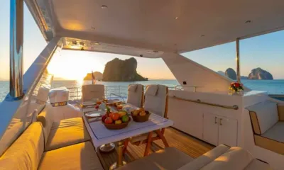 Ajao: Mesa sombreada no deck superior com frutas em tigelas e lugares postos ao pôr do sol, ilhas ao fundo