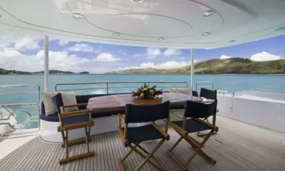 Alani: Shaded aft deck dining table with director chairs and flowers overlooking the bay