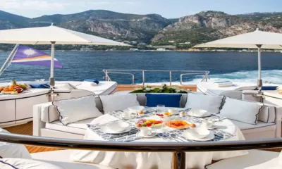 Allure: Mesa de café da manhã posta no deck de popa sob guarda-sóis, com o mar e o litoral ao fundo