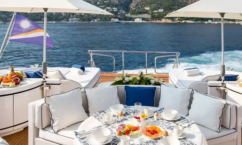 Allure: Mesa de café da manhã posta no deck de popa sob guarda-sóis, com o mar e o litoral ao fundo