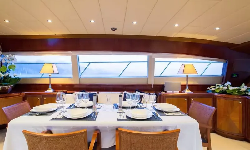 Allure: Mesa de jantar interna posta com pratos brancos e taças sob janelas longas
