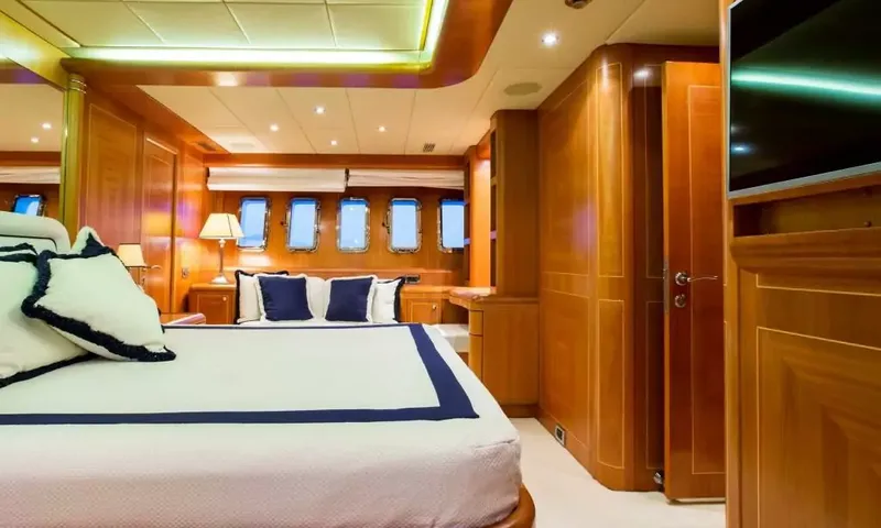 Allure: Cabine revestida de madeira com cama grande, almofadas azul-marinho, vigias e tela de parede