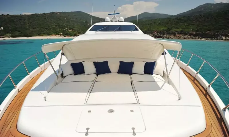 Allure: Colchonete de sol no convés de proa com toldo e almofadas, baía turquesa e colinas verdes à frente