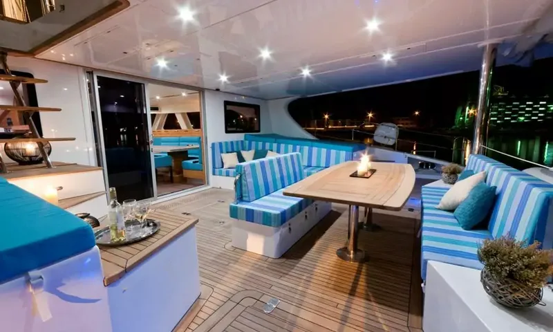 Anini: Covered aft deck at night with striped blue sofas, a wooden table and candles