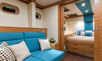 Anini: Cabin sitting area with blue sofa and portholes, opening onto a double bed with blue cushions