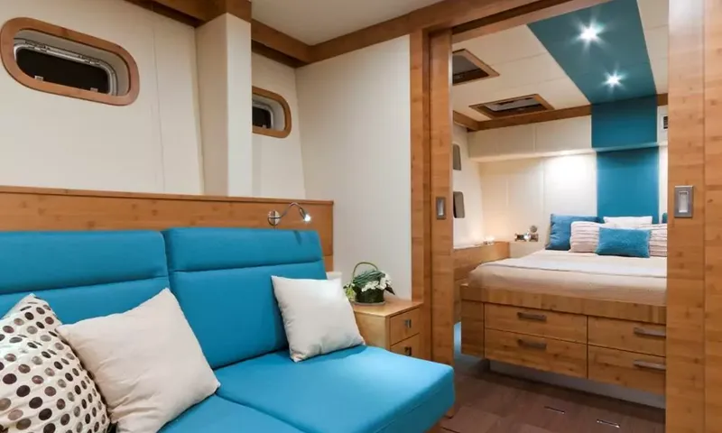 Anini: Cabin sitting area with blue sofa and portholes, opening onto a double bed with blue cushions