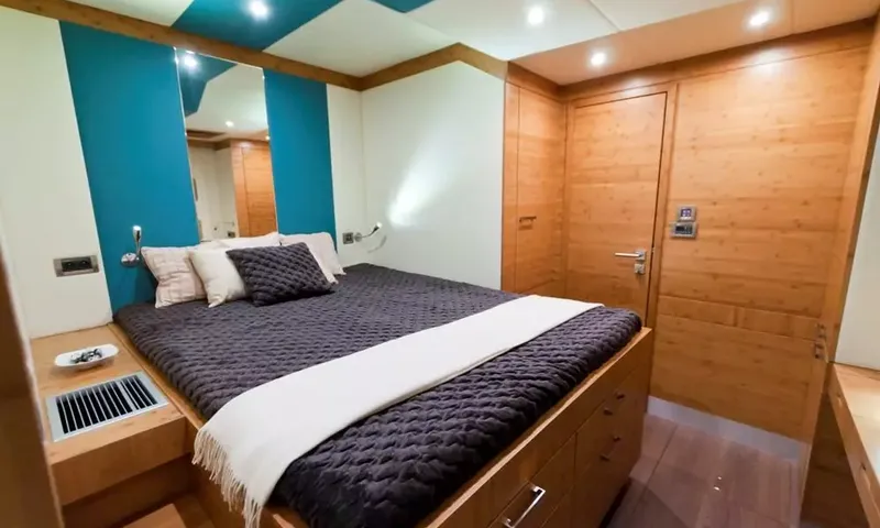 Anini: Cabin with double bed under a dark quilted cover, teal wall panels and wooden door
