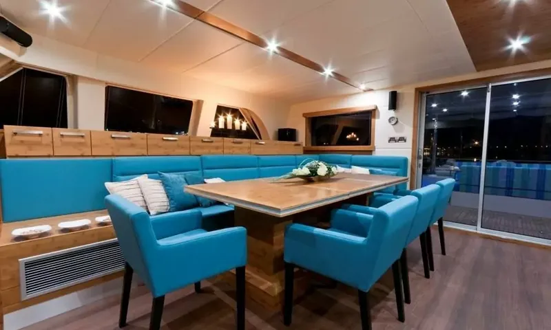Anini: Dining table with blue chairs and banquette beside glass doors leading to the aft deck