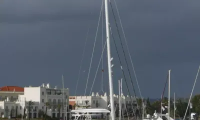 Anini: Tall sailboat masts in a marina in front of white waterfront buildings under a dark stormy sky