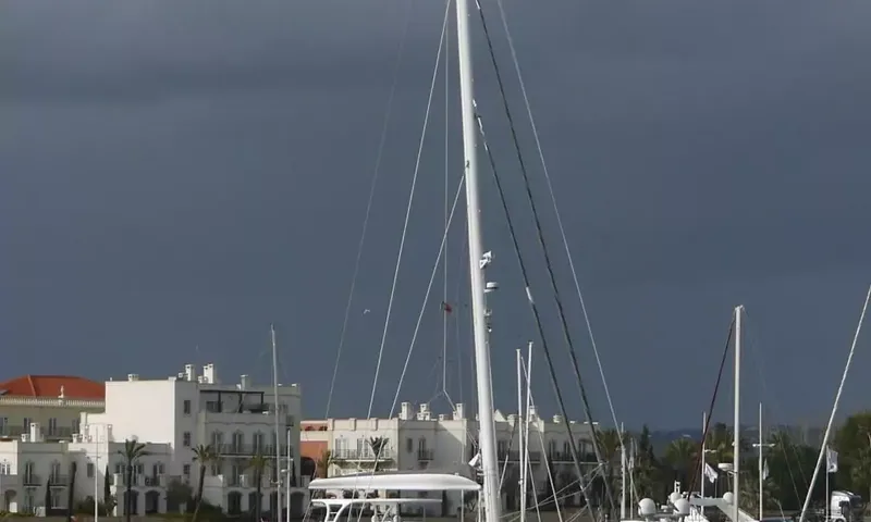 Anini: Tall sailboat masts in a marina in front of white waterfront buildings under a dark stormy sky