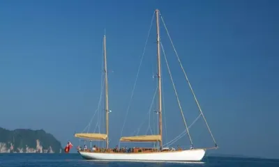 Aventure: 岩の多い岬の近く、穏やかな青い海に停泊する白い船体の2本マストのヨット