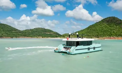 Orca: Catamarã ancorado em águas turquesa perto de colinas verdes, um pequeno barco passando em alta velocidade e uma prancha de stand up paddle ao lado