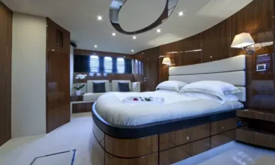 D5: Cabina con grande letto matrimoniale, pareti rivestite in legno, lampade da parete e divano sotto i finestrini