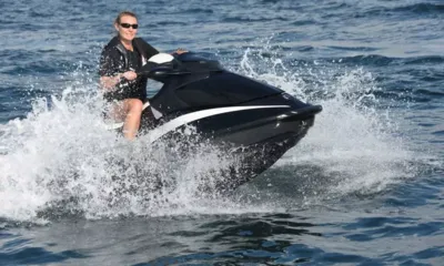 Double D: Mulher de óculos escuros pilotando um jet ski preto em meio a respingos de água do mar