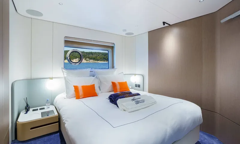 Getaway: Double cabin with orange cushions, folded towels on the bed and a porthole window