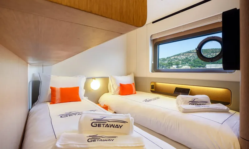 Getaway: Twin cabin with two single beds, orange cushions, towels and a window onto a hillside