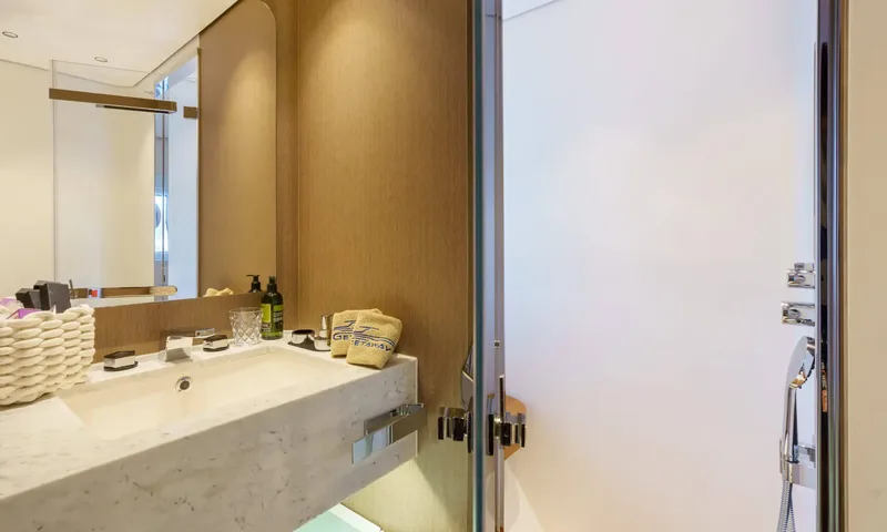 Getaway: Marble basin with toiletries and folded towels beside a frosted glass shower door