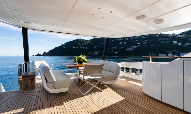 Getaway: Covered teak aft deck with armchairs and a table with flowers facing a wooded coast