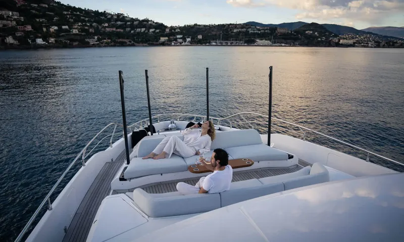 Getaway: Couple relaxing on foredeck sofas at sunset near a hillside town