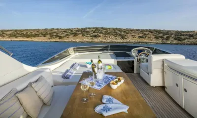 Gorgeous: Flybridge avec table dressée avec du vin, salon et poste de barre face à un rivage rocheux