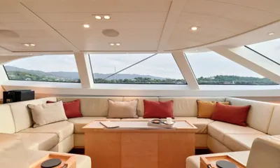 Guillemot: Lounge da timoneira com sofá creme em formato envolvente, almofadas vermelhas e amplas janelas para a costa