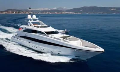Jems: Yacht bianco in navigazione vicino a una costa collinare con una piccola barca che segue