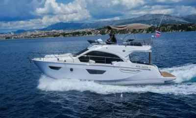 Jupika II: Vue latérale d'un yacht blanc avec flybridge filant le long de la côte, avec des montagnes en arrière-plan
