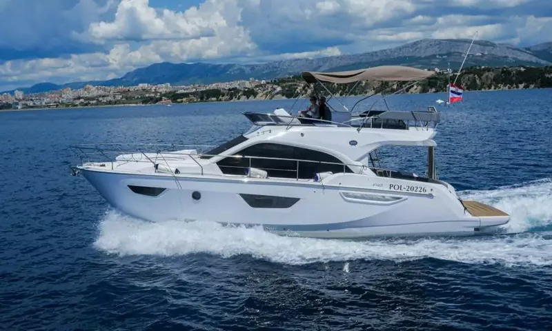 Jupika II: Vue latérale d'un yacht blanc avec flybridge filant le long de la côte, avec des montagnes en arrière-plan
