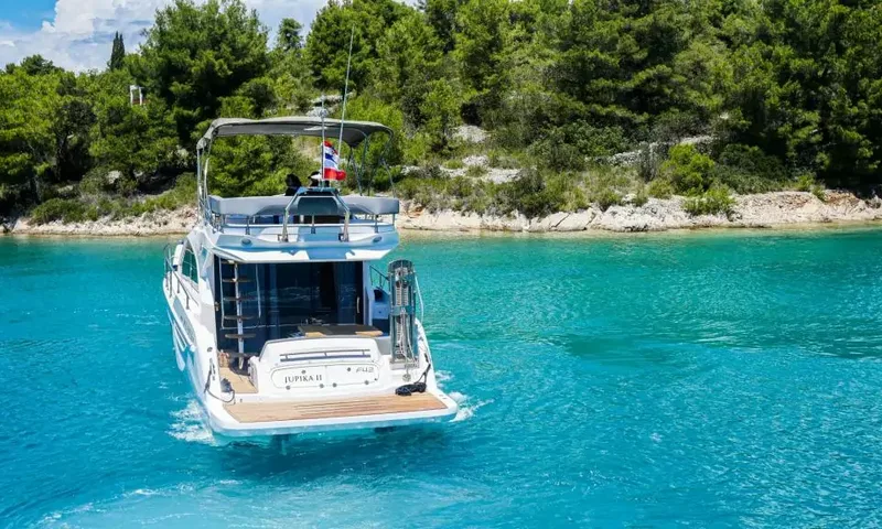 Jupika II: Vue arrière d'un yacht dans une eau turquoise près d'un rivage rocheux couvert de pins