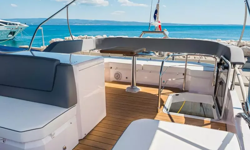 Jupika II: Flybridge avec assises à coussins gris, sol en teck et petite table face à la mer