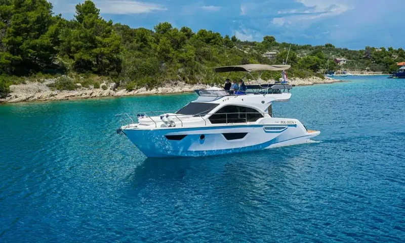 Jupika II: Yacht à moteur avec flybridge sur une eau turquoise limpide, le long d'un rivage vert et boisé