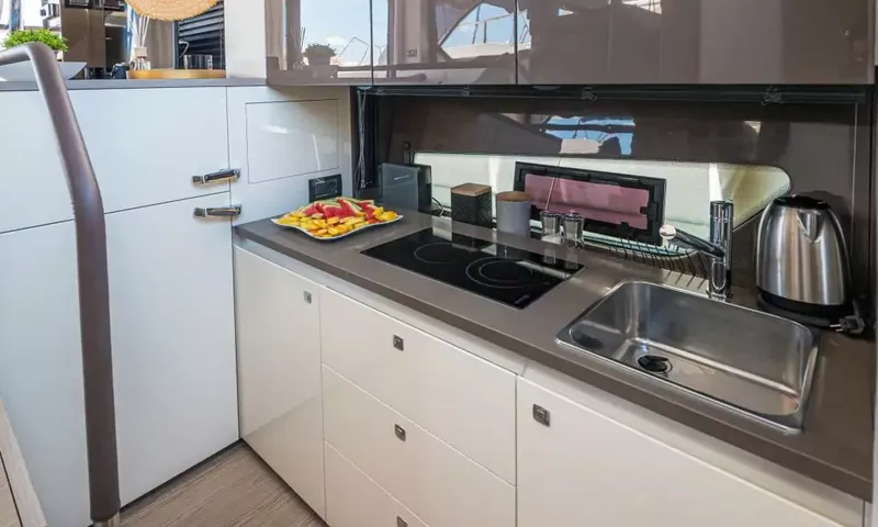 Jupika II: Plan de travail de cuisine avec plaque à induction, évier en acier, bouilloire et assiette de fruits