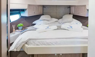 Jupika II: Cabine com cama de casal, roupa de cama branca, toalhas enroladas e armários superiores de madeira