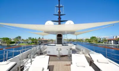 Kaos: Top deck with white sun loungers, bar stools and shade sails under a blue sky