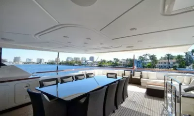 Kaos: Covered aft deck dining table with wicker chairs and a cushioned sofa along the rail