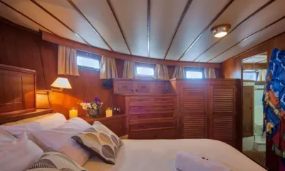 L'Orientale: Cabina rivestita in legno con letto matrimoniale, cuscini decorati, candele, armadi a persiana e porta aperta del bagno privato
