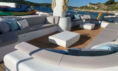 Lady Gita: Salon de pont courbe avec coussins gris et tables blanches, kayaks rangés derrière