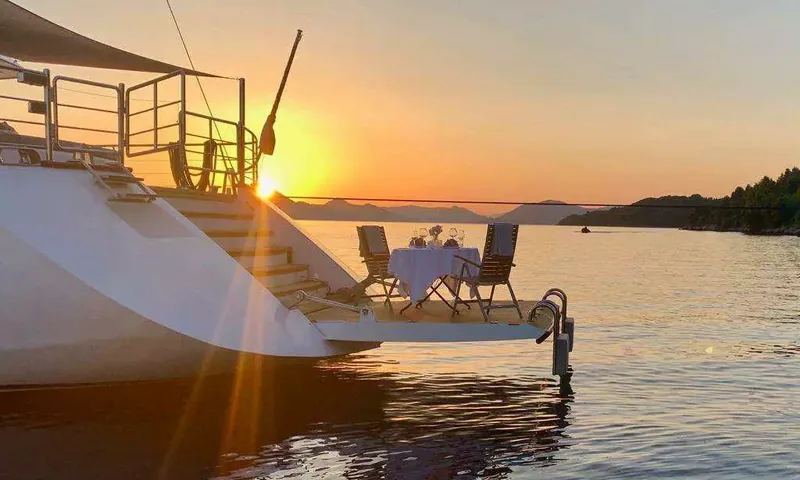 Lady Gita: Table pour deux dressée sur la plateforme arrière au coucher du soleil sur une eau calme