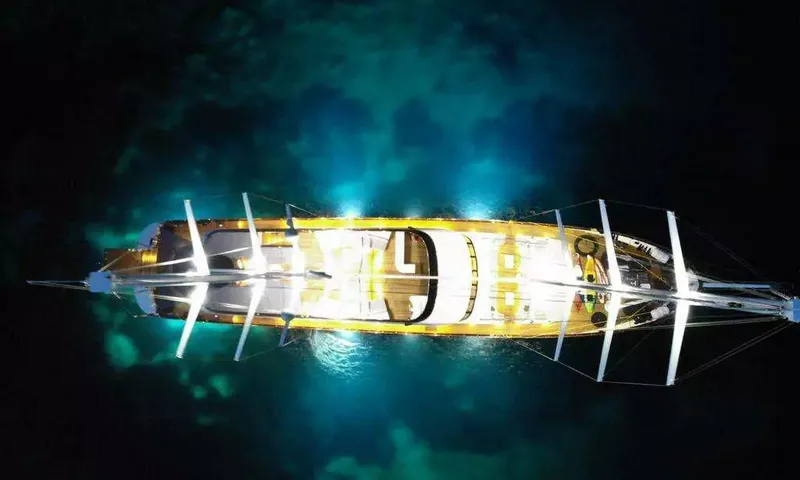 Lady Gita: Vue nocturne en plongée du yacht éclairé, ses lumières scintillant dans l'eau