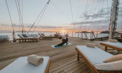 Lamima: Pessoa fazendo yoga em um deck de teca aberto com espreguiçadeiras ao pôr do sol