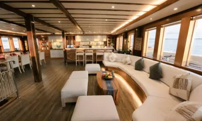 Lamima: Lounge com sofá branco curvo, pufes, balcão de bar e grandes janelas com vista para o mar