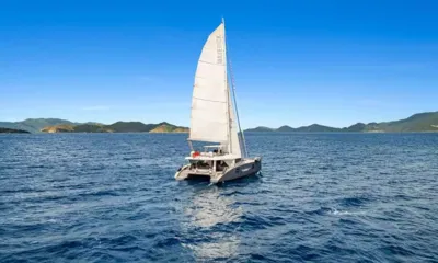 Maverick 70: メインセールを揚げ、背後に緑の丘が広がる深い青の海を帆走するカタマラン