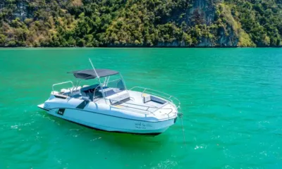 Nauti One: Barca a motore bianca all'ancora su acqua smeraldo davanti a una scogliera boscosa