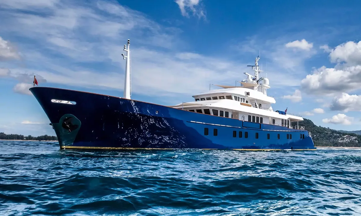 Northern Sun: Dark blue hulled motor yacht with white superstructure at anchor on choppy water near a green coast
