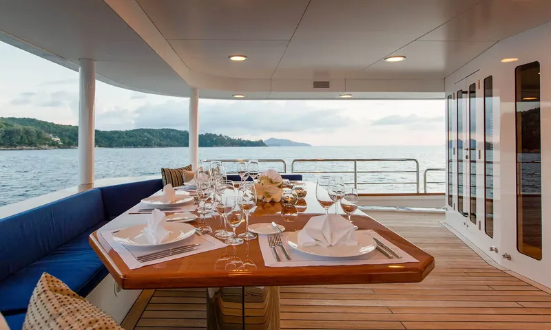 Northern Sun: Covered outdoor dining table set with plates and glasses beside blue bench seating overlooking the sea