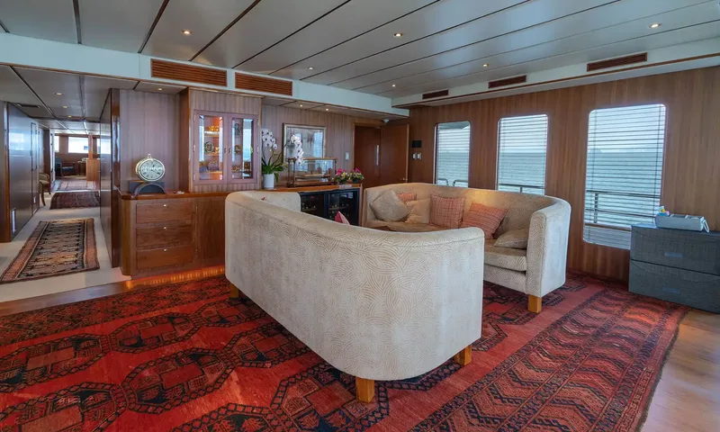 Northern Sun: Wood panelled lounge with two cream curved sofas on a red patterned rug beside windows