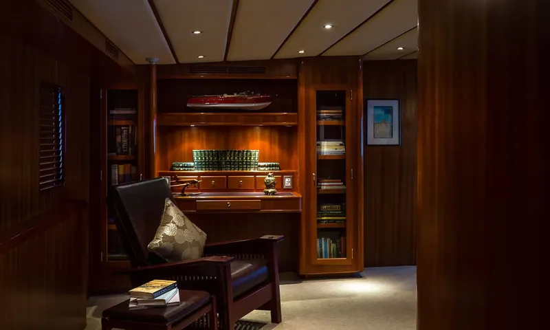Northern Sun: Dimly lit study with an armchair, bookshelves, a desk and a model boat on a shelf