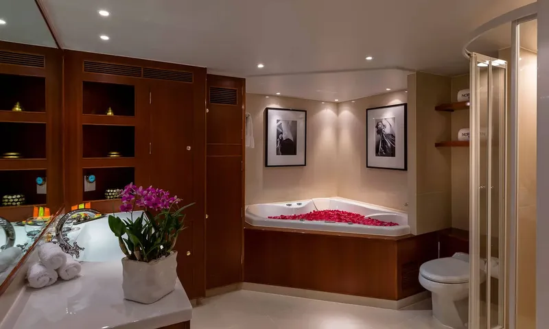 Northern Sun: Bathroom with a corner bathtub strewn with petals, a shower, toilet and a vanity with orchids