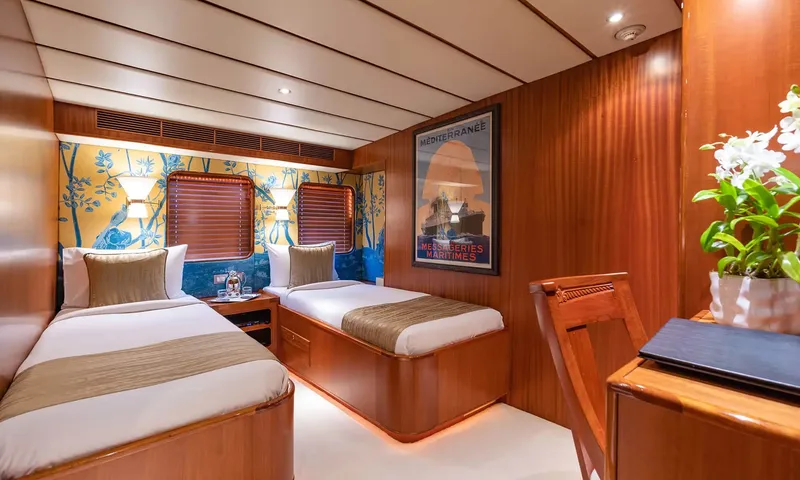 Northern Sun: Twin cabin with two single beds, blue and gold wallpaper and a framed travel poster