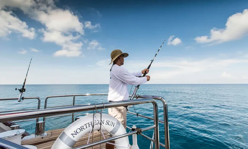 Northern Sun: Man in a hat fishing with a rod from the stern rail beside a life ring